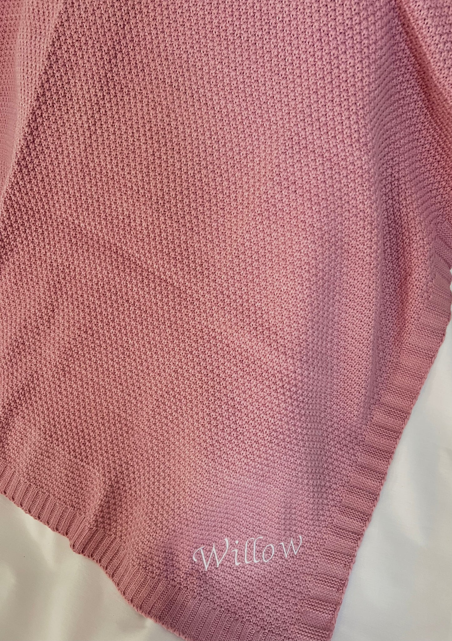 Draped personalised dusky pink fine knit baby blanket with Willow embroidered in white at the corner