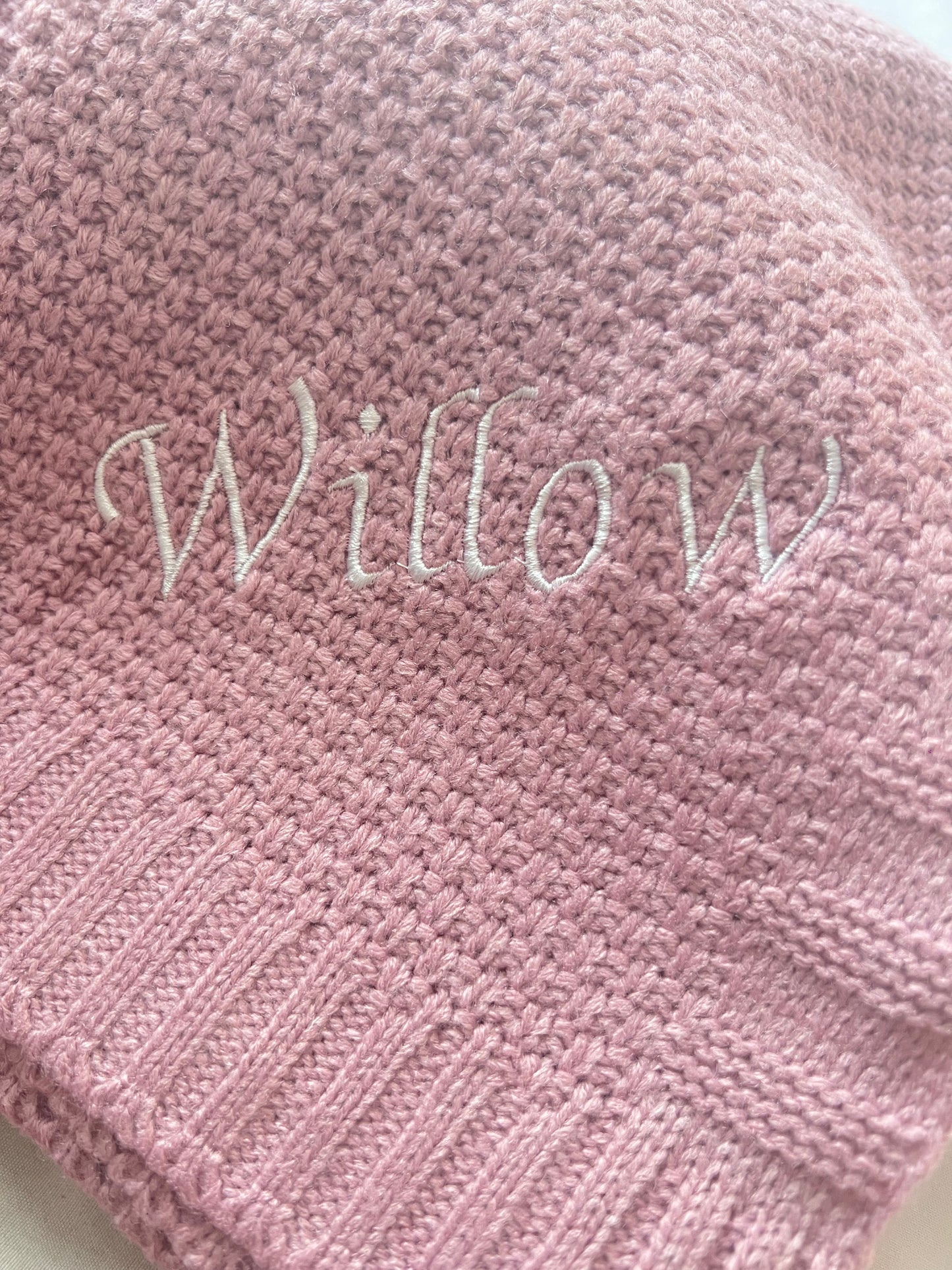 Close-up of a personalised pink fine knit baby blanket with Willow embroidered in large white script lettering