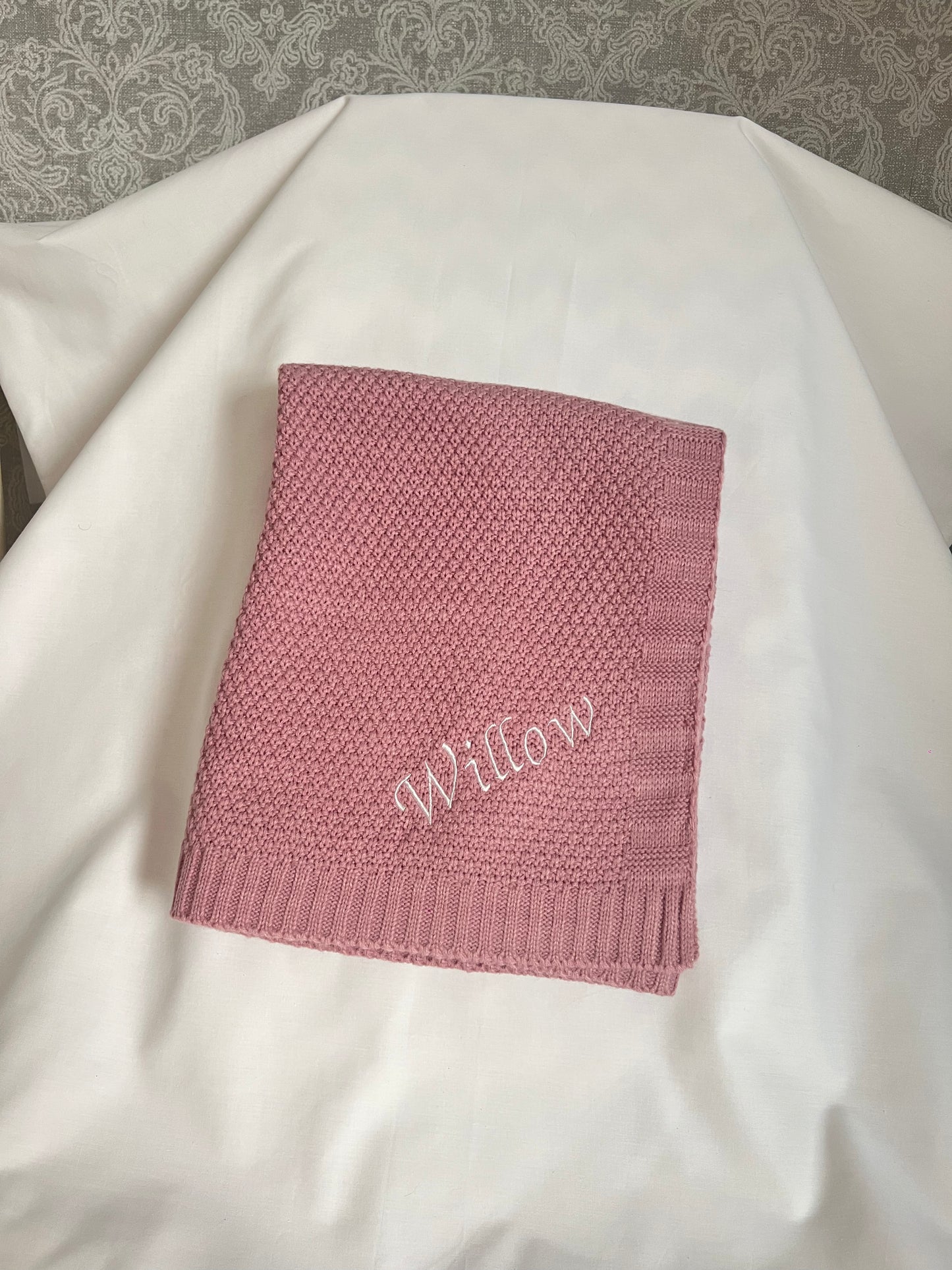 Personalised pink fine knit baby blanket with Willow embroidered in white, neatly folded on a white surface