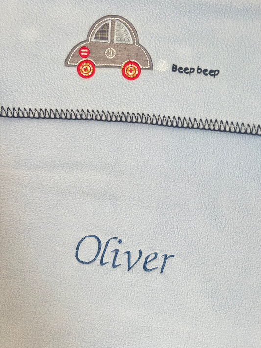Close-up of a personalised blue car seat blanket showing car appliqué embroidery and Oliver embroidered in navy thread