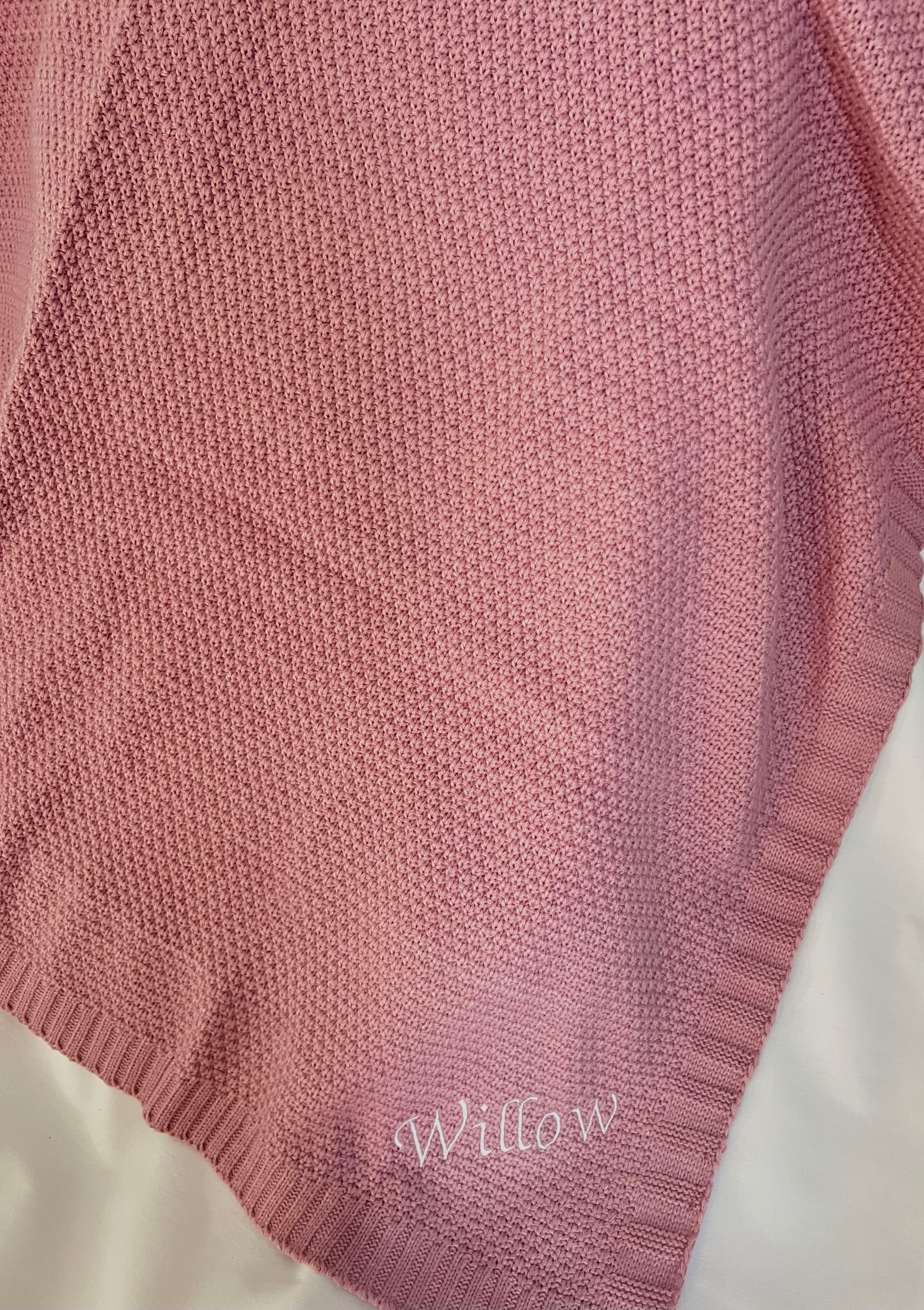 Draped personalised dusky pink fine knit baby blanket with Willow embroidered in white at the corner