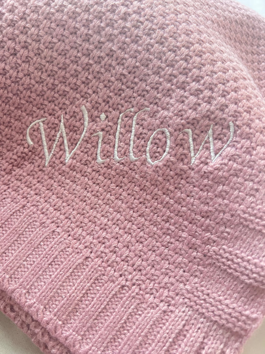  Close-up of a personalised pink fine knit baby blanket with Willow embroidered in large white script lettering